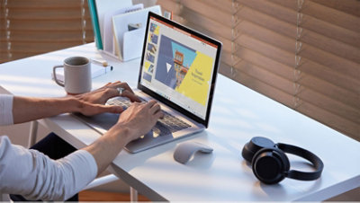 Eine Frau sitzt neben einem Tisch und tippt auf einem Surface Laptop.