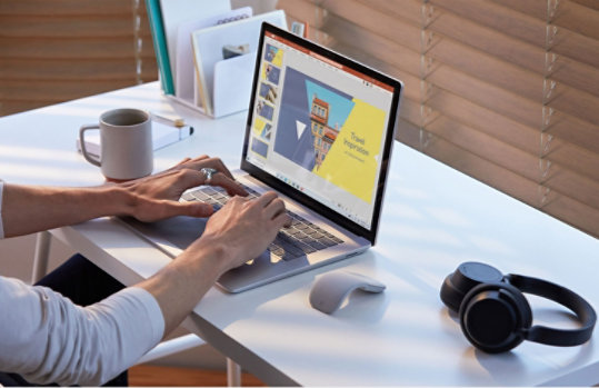 Eine  Person sitzt neben einem Tisch und tippt auf einem Surface Laptop.