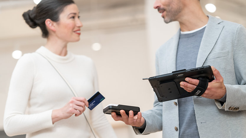 Uma pessoa a utilizar um Surface Go 4 para Empresas e diversos acessórios para concluir a transação de um cliente com um cartão de crédito.