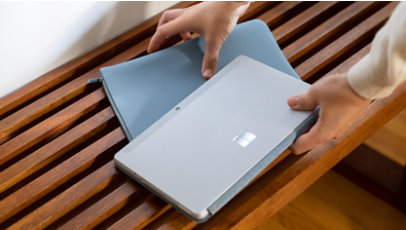 A pair of hands picking up a Surface Go and Ice Blue sleeve. 