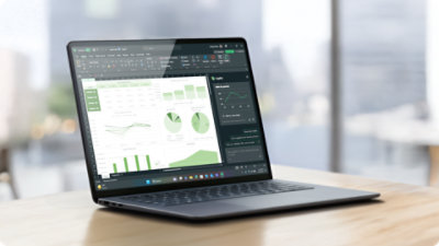 A Surface Laptop for Business sits open on a table displaying the Excel app with Copilot assisting inside a spreadsheet.