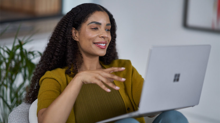 Woman sitting in a casual work environment using a platinum Surface Laptop.