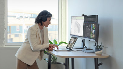 An individual standing at a desk, using a Surface Laptop Studio and Surface Headphones to get work done.
