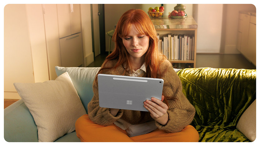 A person sits on a couch holding a Surface Pro for Business.