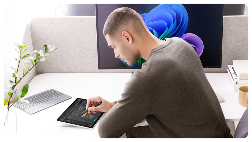 Henkilö istuu työpöydän ääressä ja kirjoittaa Surface Pro yrityksille -tietokoneella muistiinpanoja käsin käyttämällä Slim Pen -kynää. 