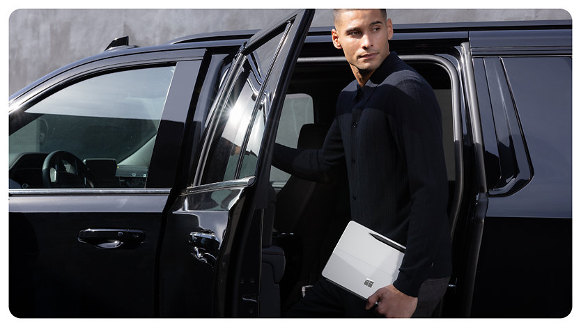 A person holds a Surface Pro for Business while getting out of a car.