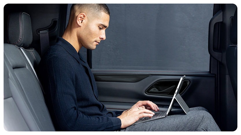 A person sits in the backseat of a car using a Surface Pro for Business with the kickstand engaged, suggesting the flexibility and portability of the device.