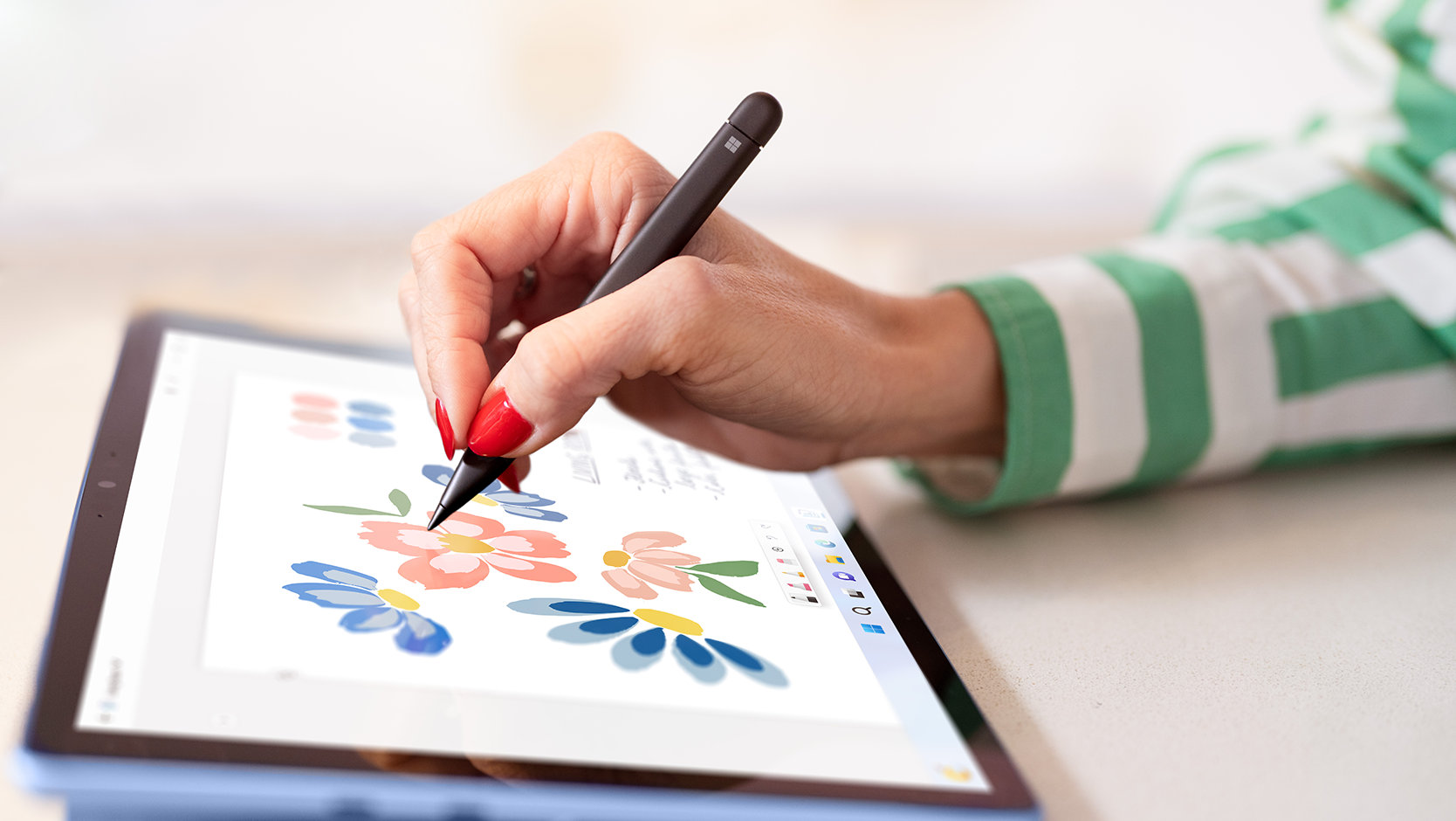 A person uses a Surface Slim Pen to draw on the screen of a Surface device, showing off the flat, comfortable design of the pen.