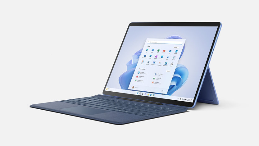 زاوية عرض 3/4 من الأعلى للابتوب Surface Pro 9 باللون أزرق ياقوتي، مع لوحة مفاتيح Surface Type Cover مرفقة.