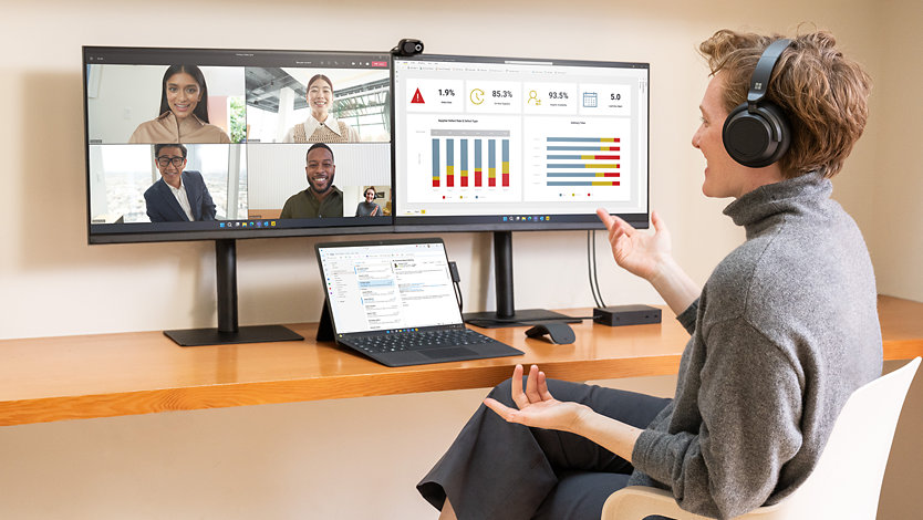 En person som ringer ett samtal via Surface Pro 9 för företag och samtidigt utför uppgifter på två externa bildskärmar.
