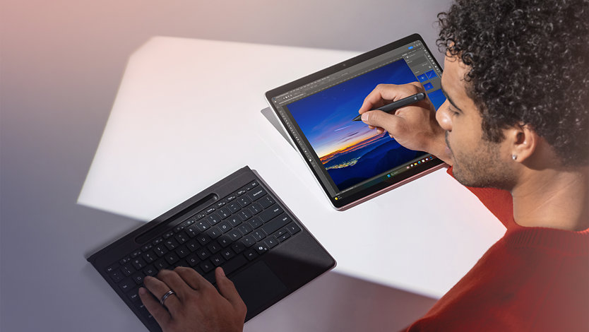 Een persoon typt op een losgekoppeld Surface Pro Flex-toetsenbord en schrijft met een Surface Slim Pen voor zakelijk gebruik op het touchscreen van een Surface Pro voor zakelijk gebruik-apparaat. 