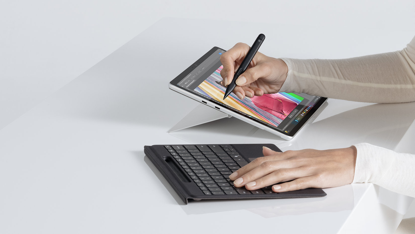 A person uses a Surface Slim Pen for Business to draw on the screen of a Surface device, and also uses a detached Surface Flex Keyboard for Business. 