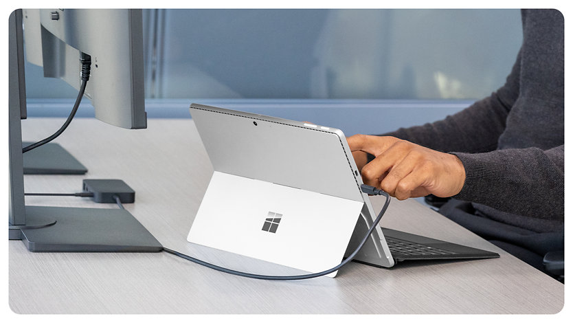 Une personne connecte une Surface Pro à un appareil Station d’accueil Surface USB4 pour les entreprises, sur son bureau.