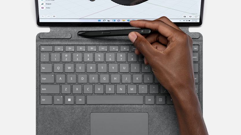 Hand lifting Surface Slim Pen 2 from Surface Pro Signature Keyboard in Platinum.