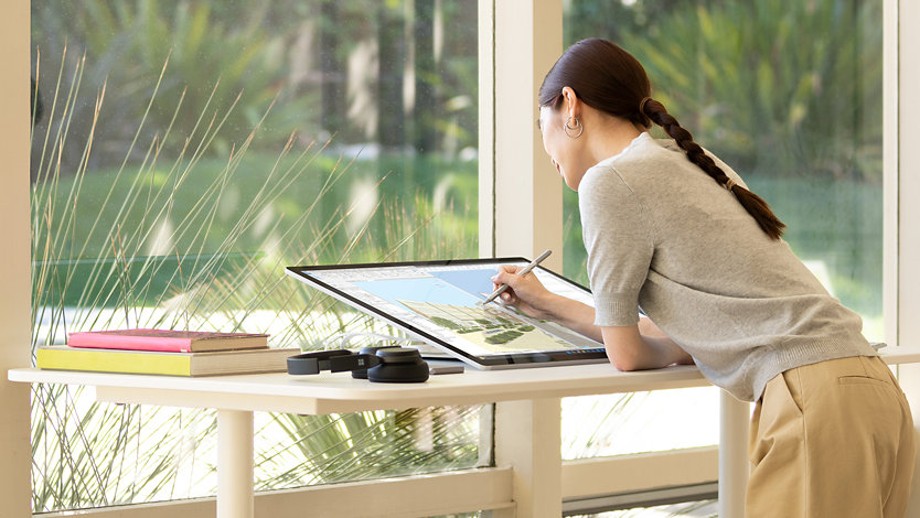 A person writes on the screen of a Surface for Business device while standing at a desk.