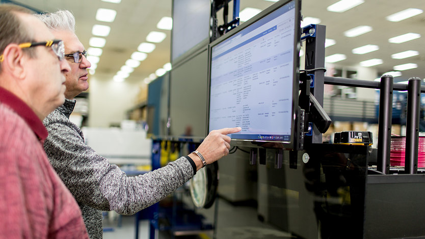 Employees review data securely on computer monitors in a warehouse. 