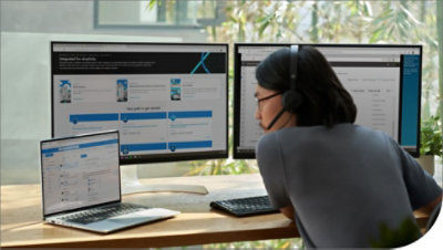 Osoba koja radi za stolom sa više monitora i slušalicama sa mikrofonom.