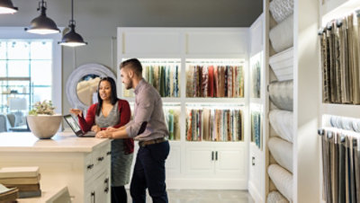Two people standing at a counter in a fabric showroom and looking at a laptop.