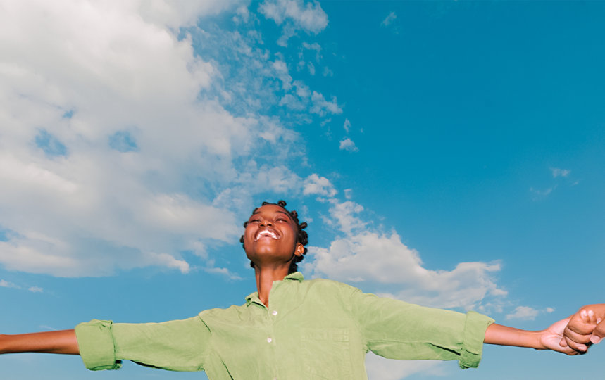 Woman laughing while holding hands with her friends under a blue sky