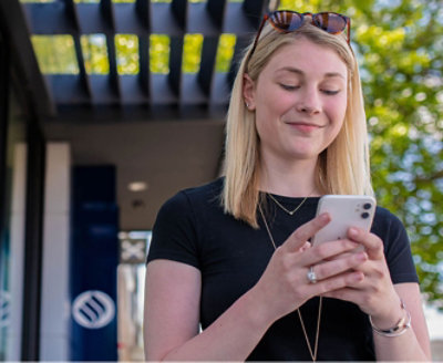 Una mujer mira su teléfono fuera de un edificio.