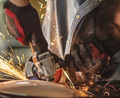 Un hombre usando una herramienta de corte manual con guantes y las chispas saltando