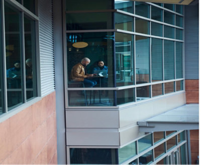 Two people sitting at a table with laptops in front of a window