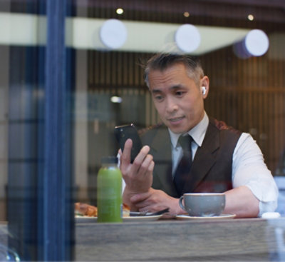 A man in a vest sits at a cafe table, looking at his phone.