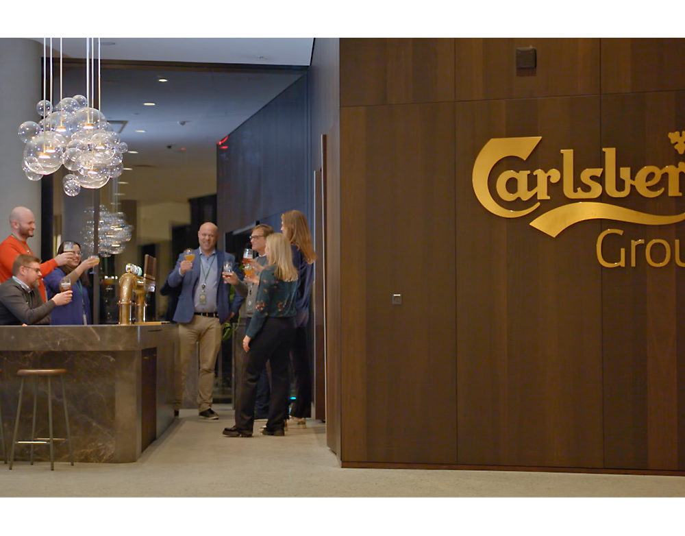 People conversing near the entrance of the carlsberg club, with one man serving drinks.