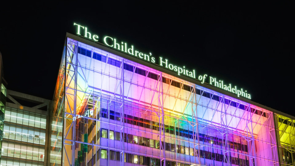 Front of Children’s Hospital of Philadelphia building at night lit up with multicolored lights.