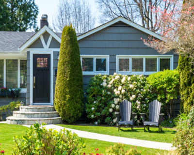 A quaint suburban house with a well-manicured garden, featuring two chairs on the lawn and vibrant flowering 