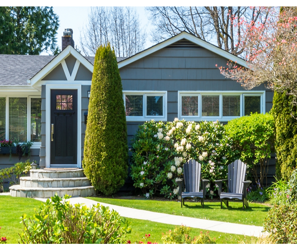 Приятный пригородный дом с ухоженным садом с двумя креслами на лужайке и яркими цветами 
