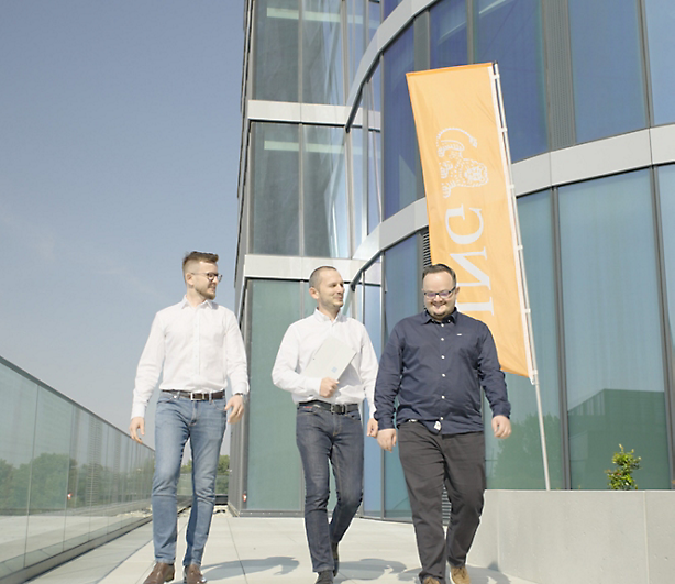 Three men walking in front of a building with ING logo banner on it.