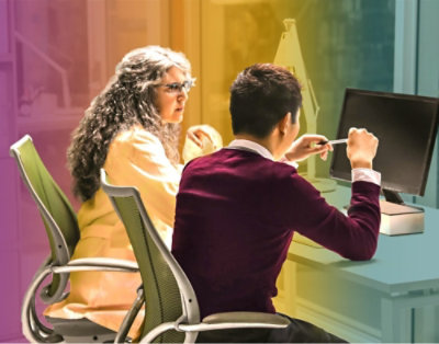 Čovek i još jedna osoba sede za stolom i gledaju u ekran računara.