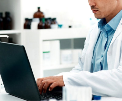 A person in a lab coat typing on a computer
