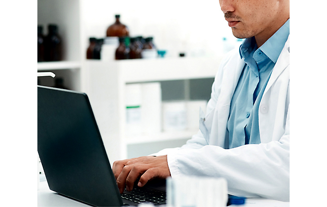 A person in a lab coat typing on a computer