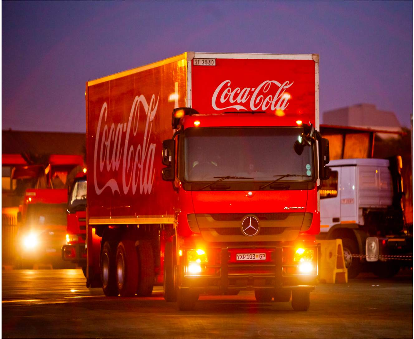 Egy piros coca cola teherautó egy parkolóban áll.