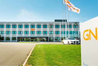 Modern office building with "gn" logo, lush green lawn in the foreground, two flags waving under a clear blue sky.