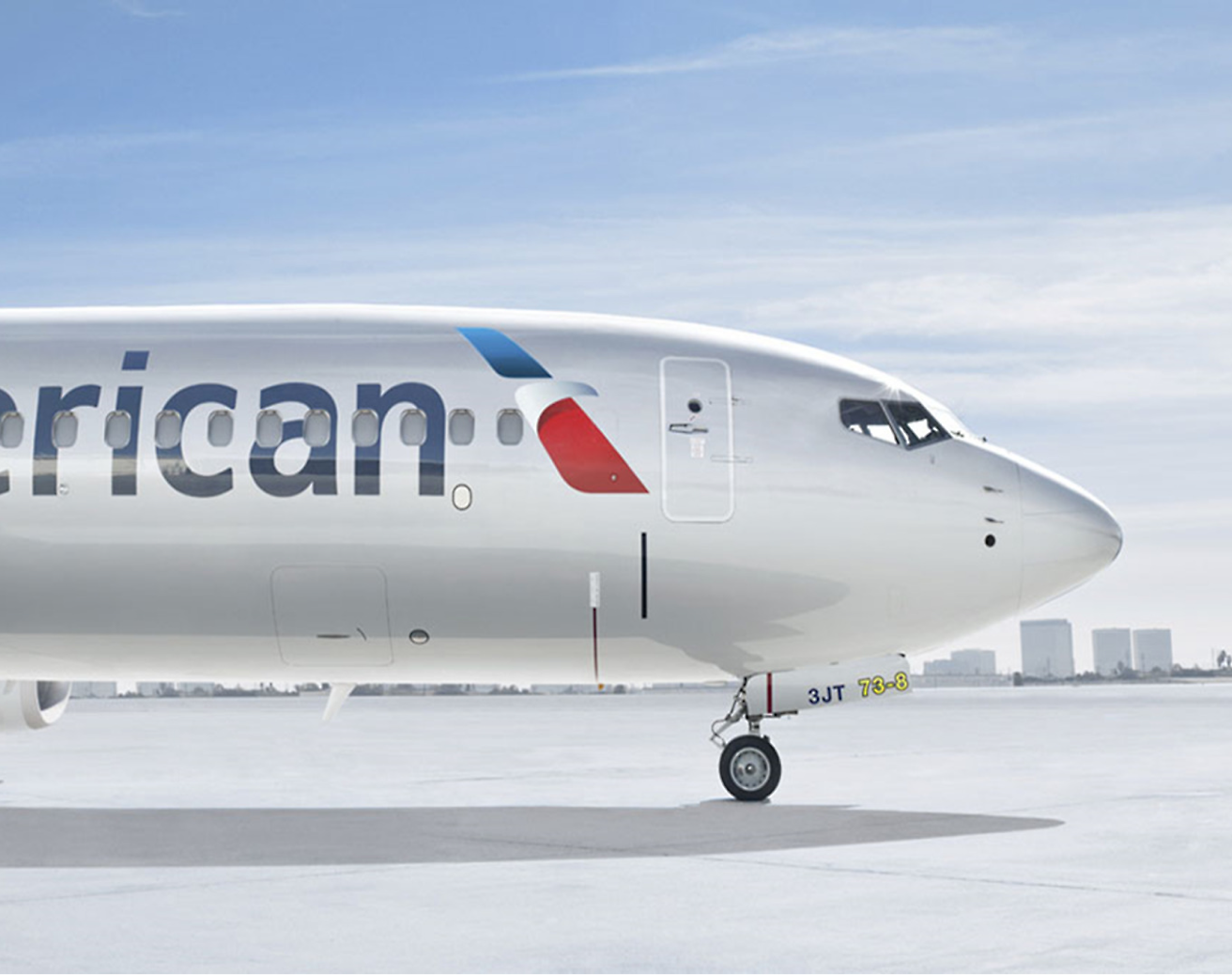 En frontvisning av et American Airlines-fly parkert på rullebanen under en skyfri himmel.