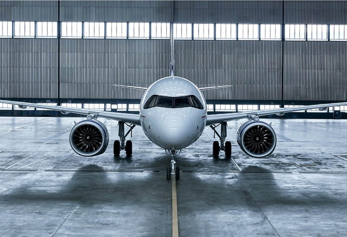 A commercial jet parked inside a hangar, facing forward with open hangar doors in the background.