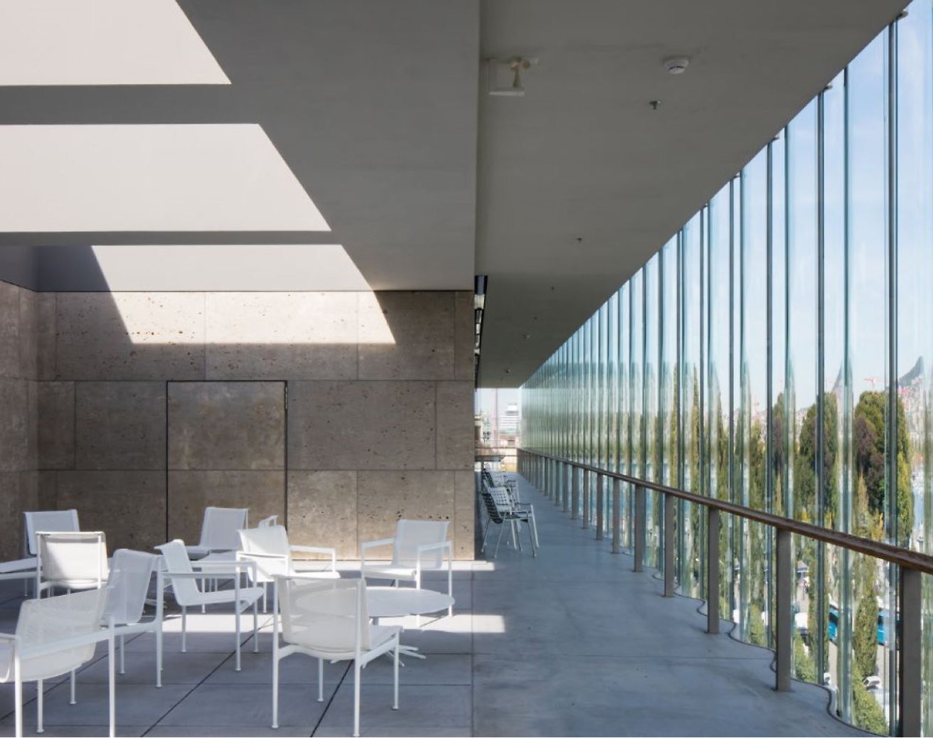Moderna terraza exterior con sillas y mesas blancas, con grandes ventanas de cristal y sombras geométricas