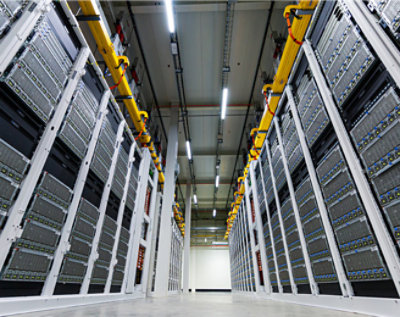 Aisle between rows of tall, modern server racks in a data center with cable trays overhead.