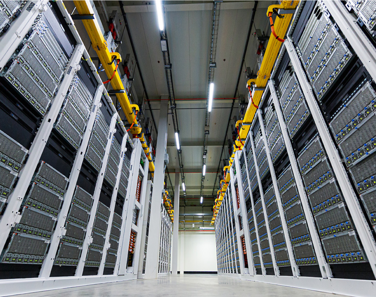 Corredor entre fileiras de racks de servidores altos e modernos em um data center, com bandejas de cabos suspensas.