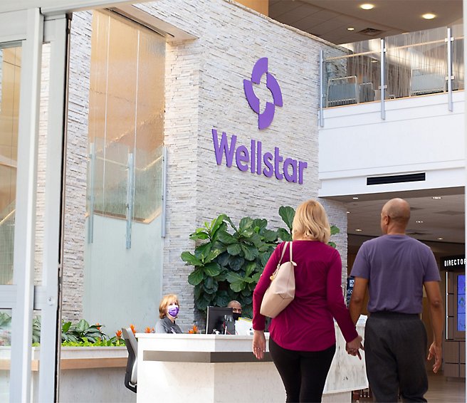 Two people walking in front of the reception at Wellstar.