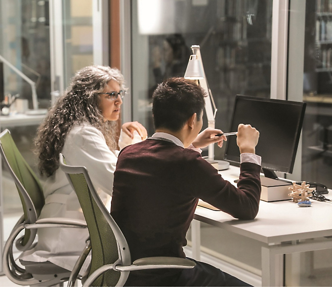 Ένα άτομο και ένα άλλο άτομο κάθονται σε ένα γραφείο, κοιτάζοντας μια οθόνη υπολογιστή