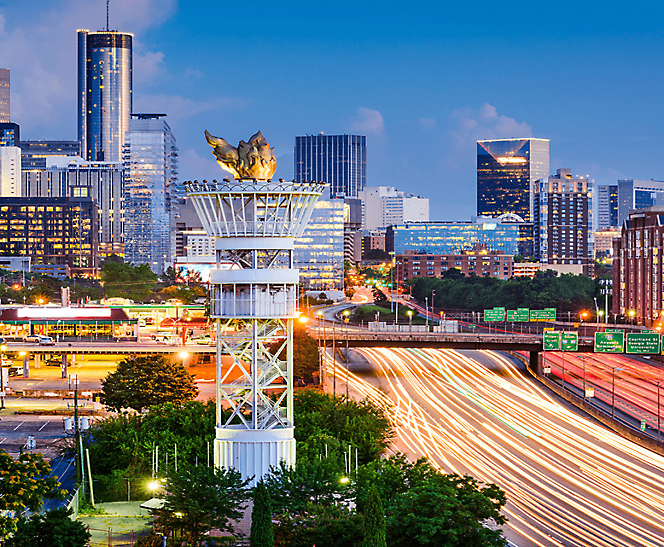 Horizonte urbano de Atlanta al atardecer con la torre de la linterna olímpico y el tráfico ocupado de la autopista.