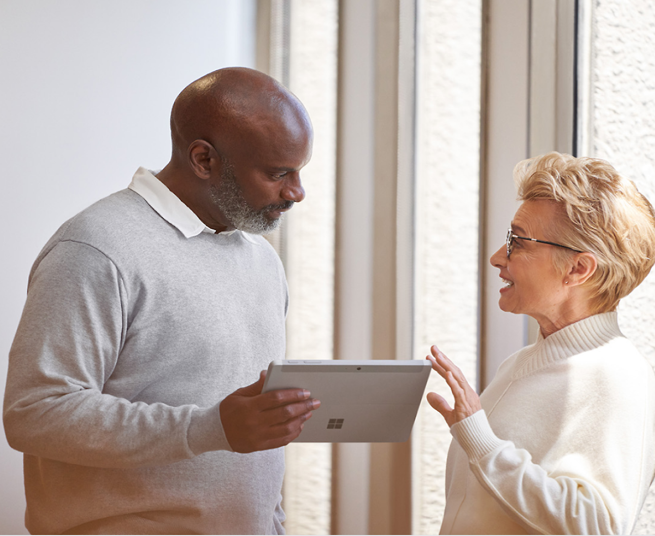 A man holding a surface pro talking to a woman