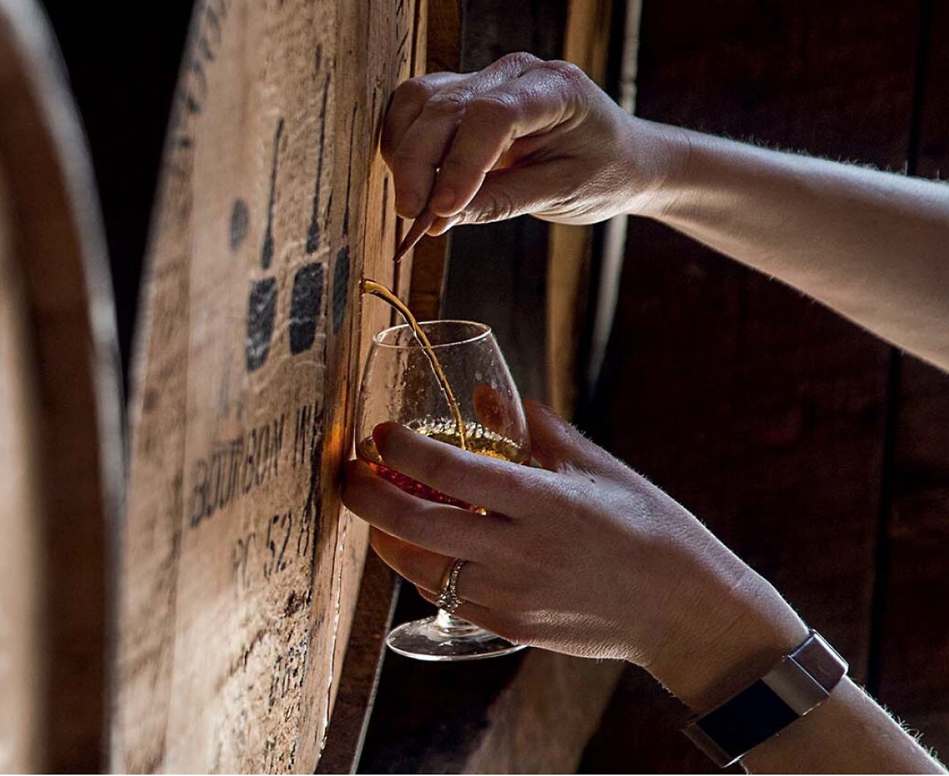 A person pouring a glass of whisky from a barrel.