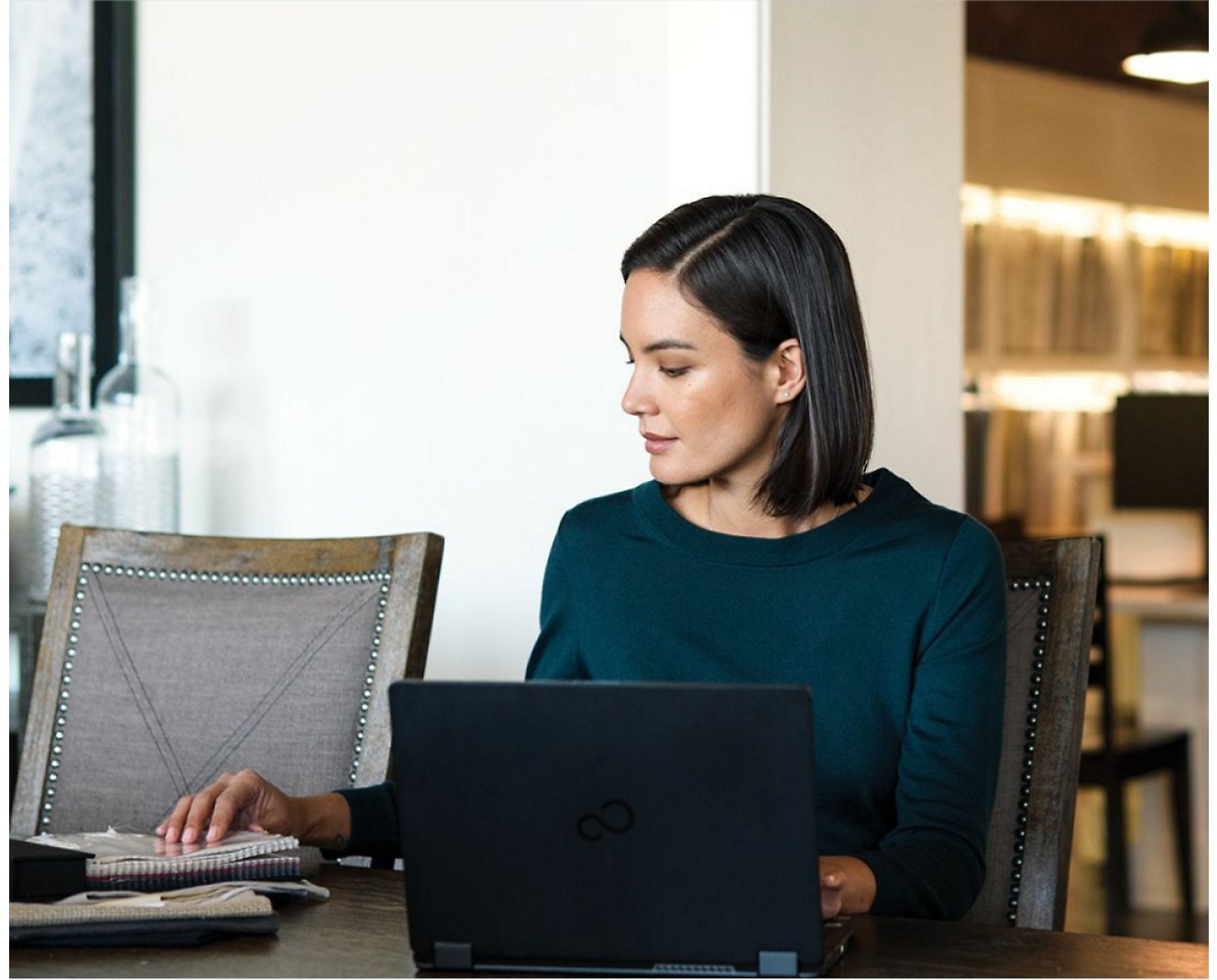 Uma mulher trabalhando em seu laptop e também em cadernos colocados em sua mesa