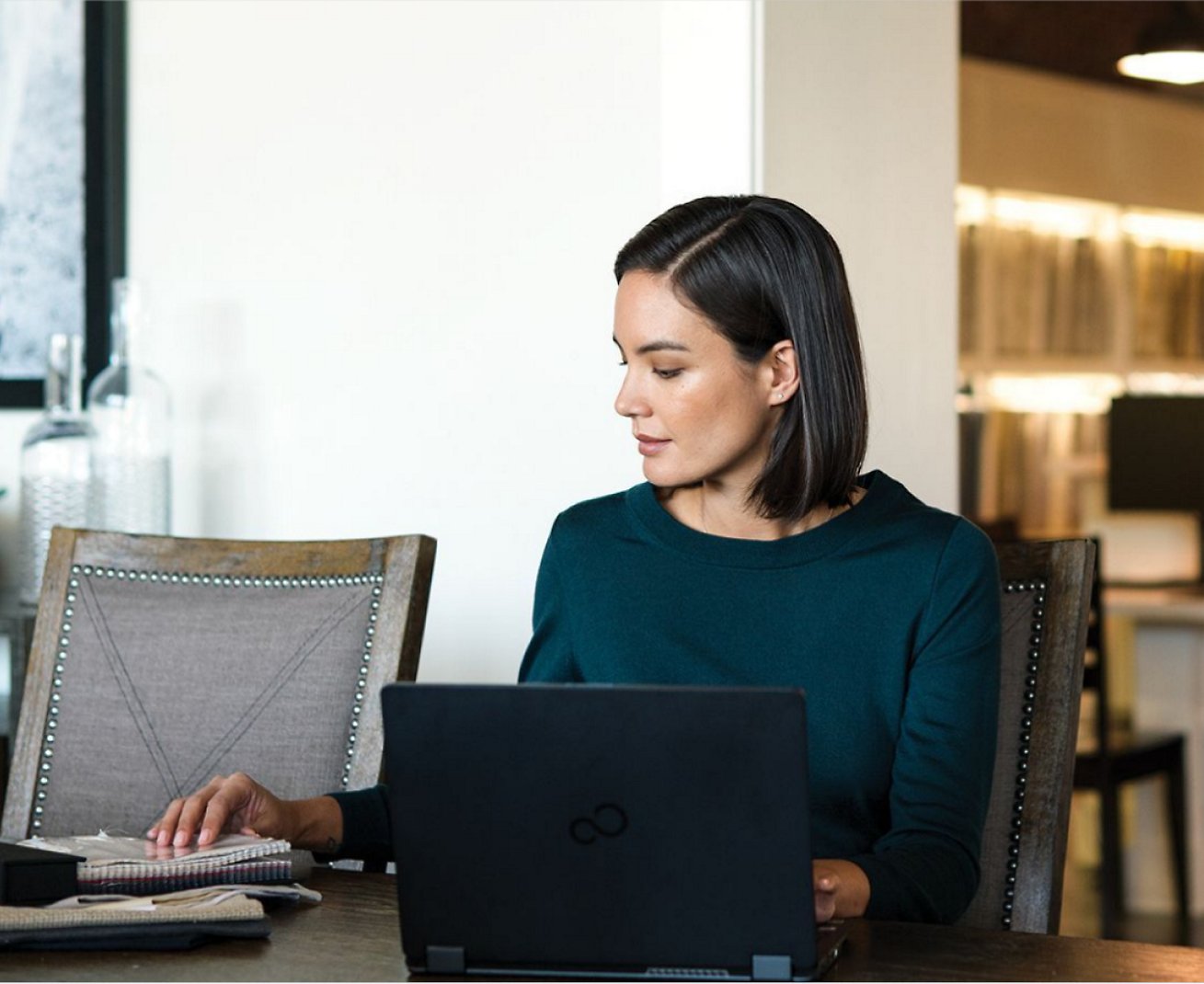 Uma mulher trabalhando em seu laptop e também em cadernos colocados em sua mesa