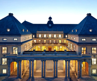 A grand building illuminated at twilight with a classical facade and a double staircase.